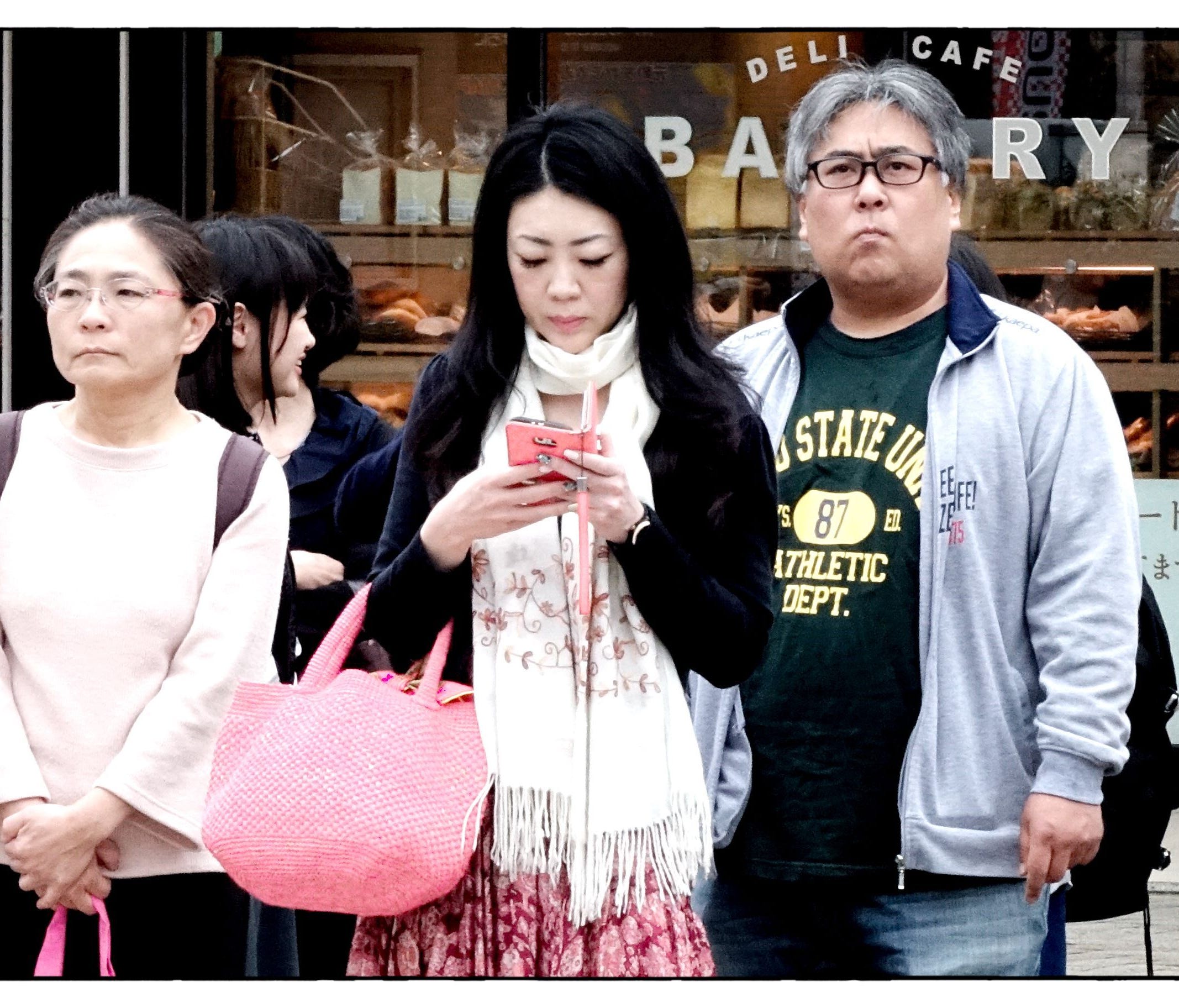 A woman checks her smartphone while walking down the street in Kobe, Japan