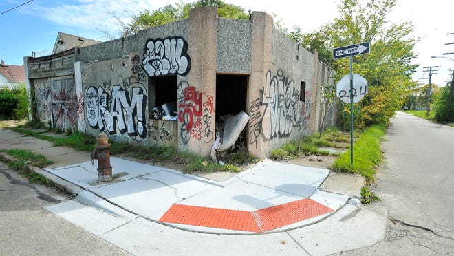 Handicap accessible corner curbs along Warren East at Elmwood in front of a burnt out building and unusable sidewalks due to debris and foliage in Detroit.