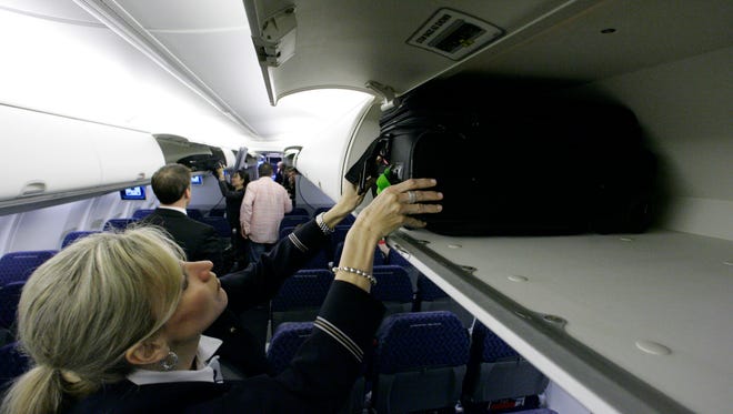 An American Airlines flight attendant  demonstrates stowing a bag in an overhead bin.