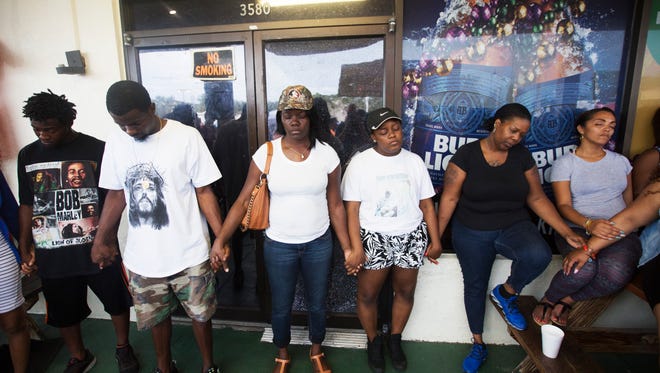 People take part in a prayer service in front of Club Blu in Fort Myers Monday.  It was the scene of a mass shooting that took the lives of two teens and injured at least 16.  