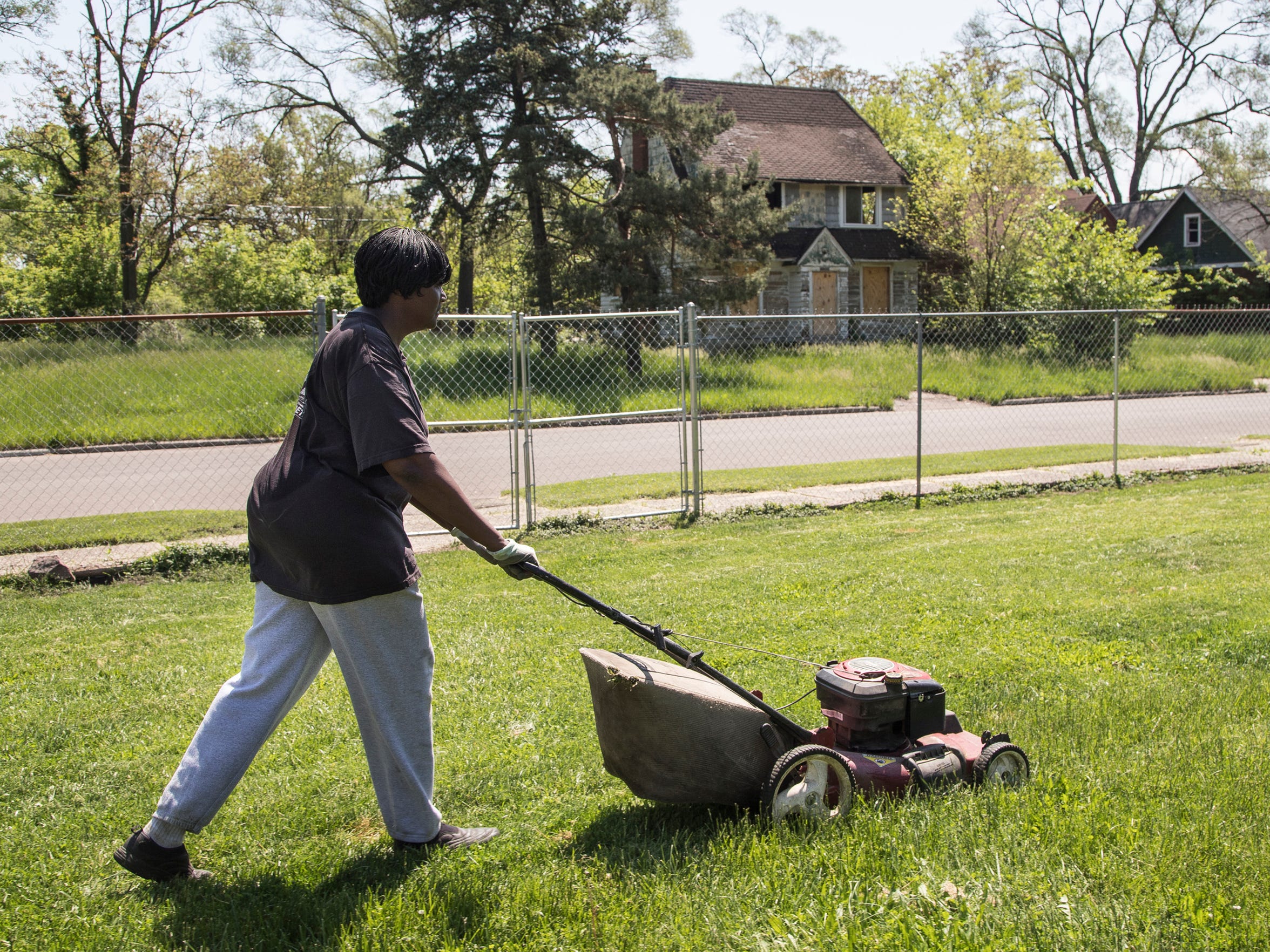 Anna Hollins in May mows the yard of her Lauder Street home, which sits across from a land bank house investigated for possible dog fighting. (Photo taken May 25, 2018)