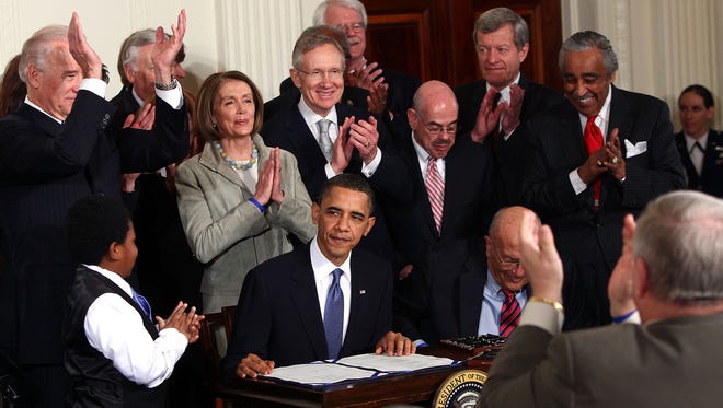House Speaker Nancy Pelosi and Senate Majority Leader Harry Reid applaud as President Obama signs the health care law in 2010.