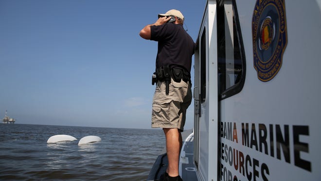 Lt. Jason Downey, of the Alabama Department of Conservation and Natural Resources, calls in a capsized catamaran as search and rescue operations continue  off Dauphin Island, Ala. on Sunday, April 26, 2015. Coast Guard crews continued searching Sunday for five people missing in the water after recovering two bodies following a powerful storm that capsized several sailboats participating in a regatta near Mobile Bay, Ala.