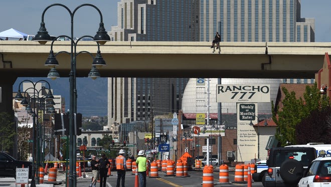 People gather on Fourth Street as they watch a man sitting on the edge of the Wells Avenue bridge early morning on Friday, May 4, 2018. Reno police block traffic on both sides of the street.