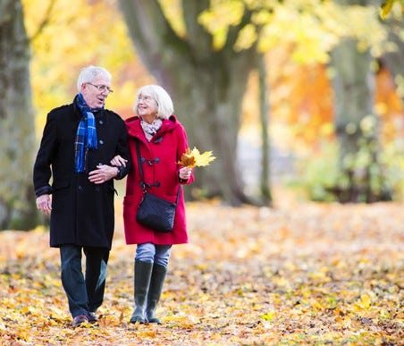 Senior couple walking in the woods with leaves on the ground in the fall