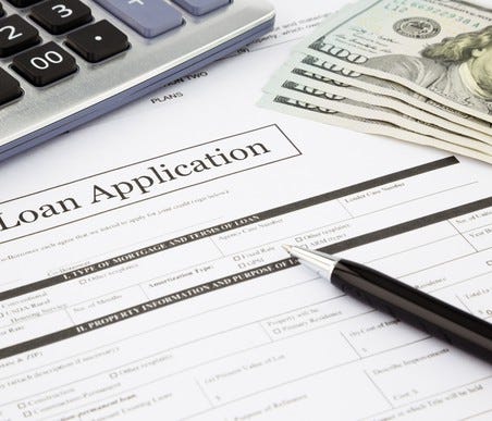 Loan application with a calculator, pen, and $100 bills on a flat surface.
