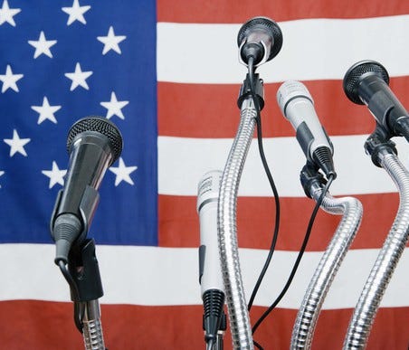 Five microphones in front of a U.S. flag.