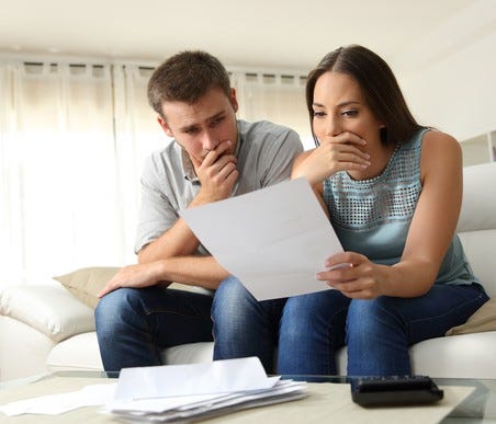 A young couple sitting on a couch and looking at a bank statement.