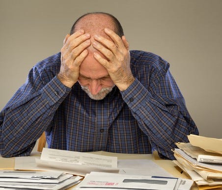 Older man looking at documents while holding his head.