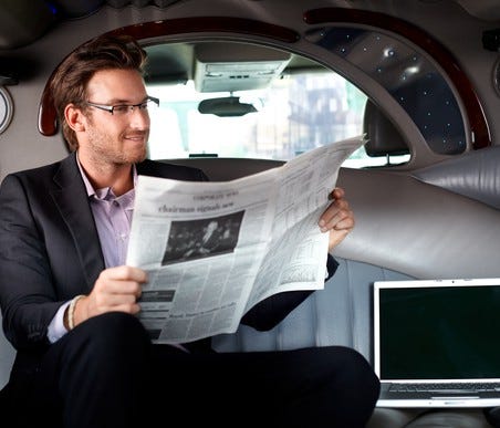 Man reading a newspaper in the backseat of a limo
