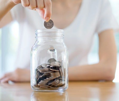 Woman dropping a coin into a savings jar.