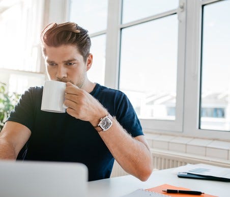 Young male adult at a laptop with mug in hand