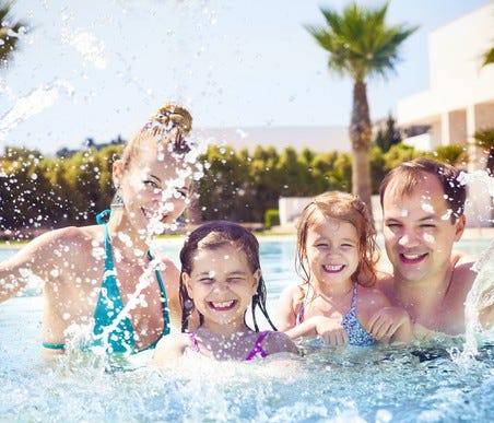 Two adults and two children splashing in a pool