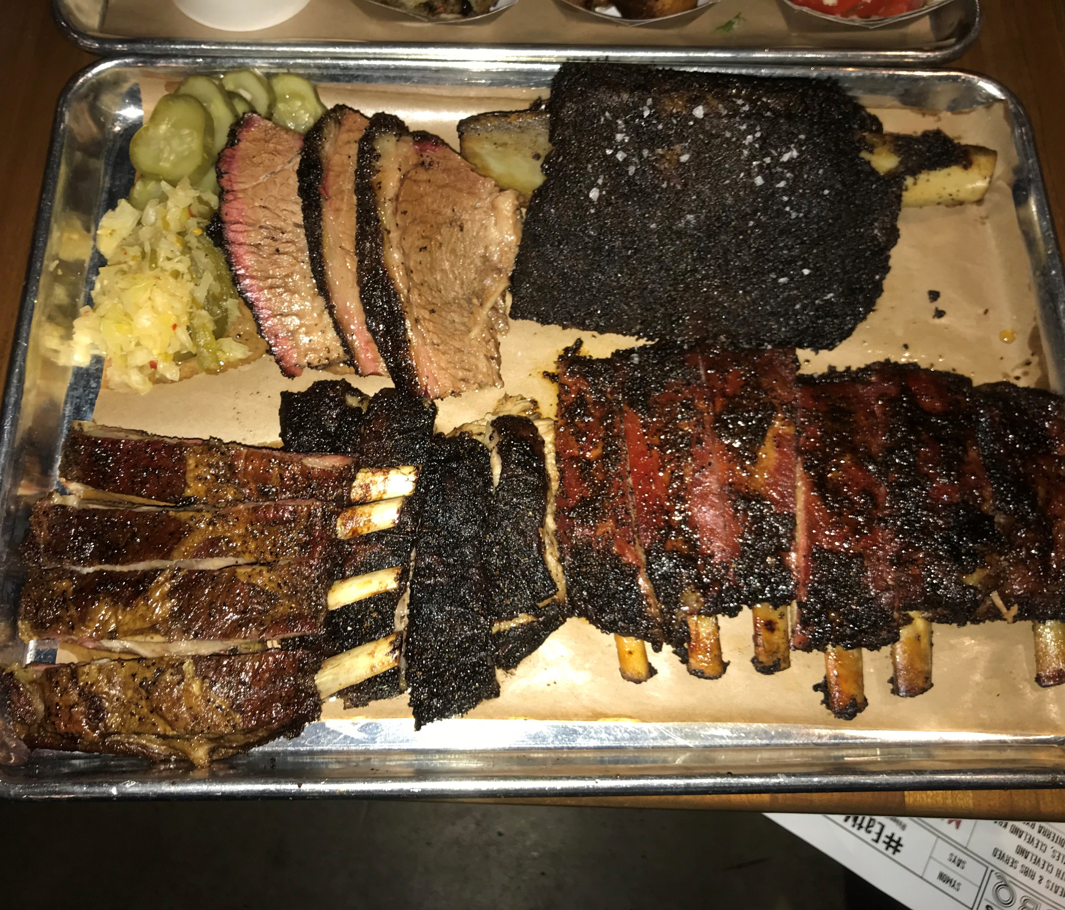 Signature slow-smoked meats include sliced beef brisket, giant beef rib, pork spare ribs, pork belly and lamb ribs (clockwise from upper left).