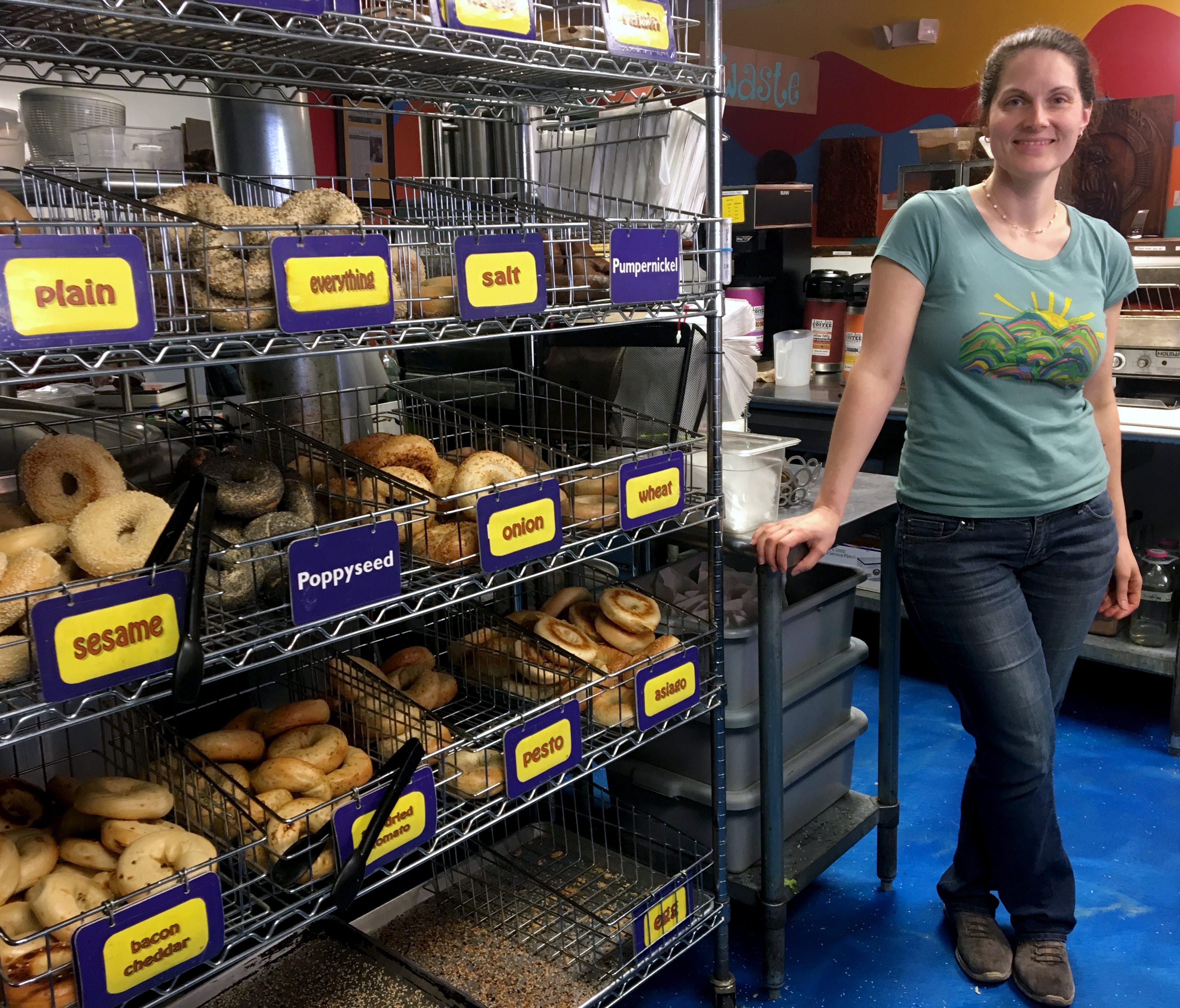 Laura Kerrone, owner of the Psychedelicatessen bagel bistro, poses beside a bagel rack at her store in Troy, N.Y. Kerrone said she looks forward to providing a payroll deduction retirement savings plan to her employees if a state-facilitated program 