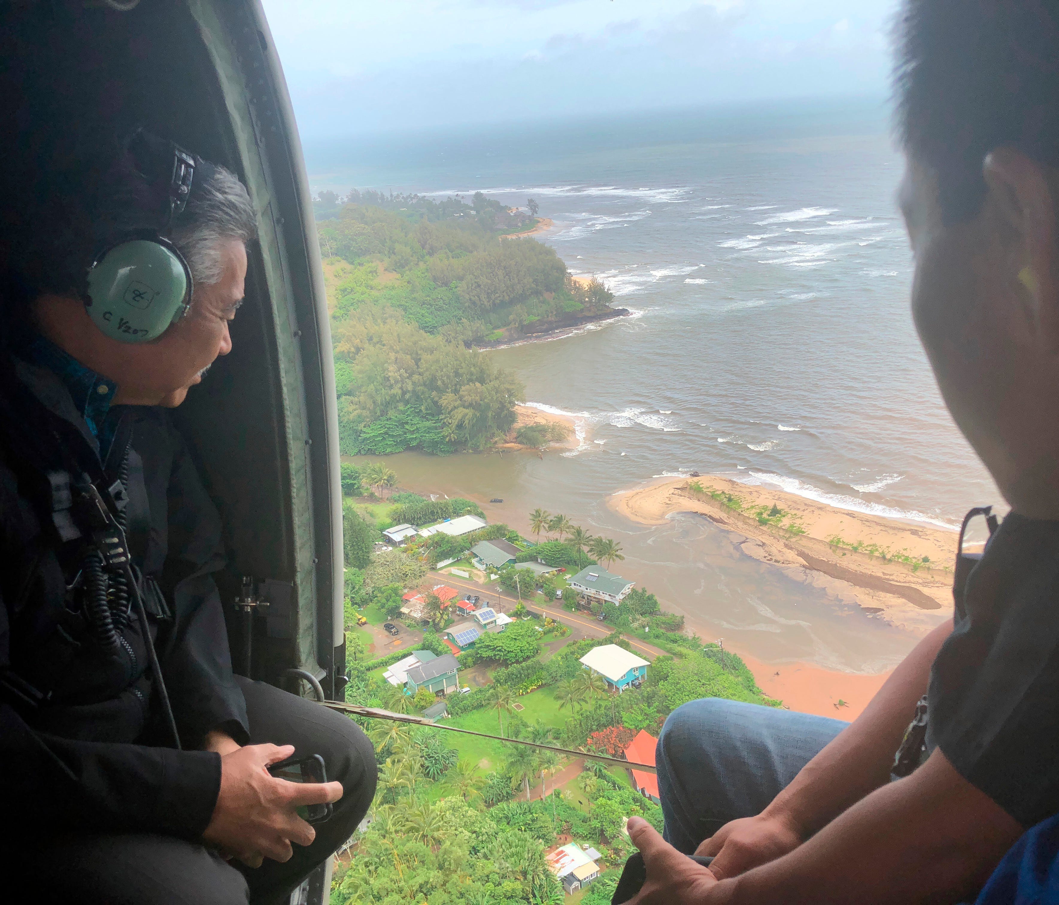 In this April 16, 2018, photo provided by the Office of the Governor, Hawaii, Hawaii Gov. David Ige, left, flies over the flood-damaged areas of the island of Kauai.