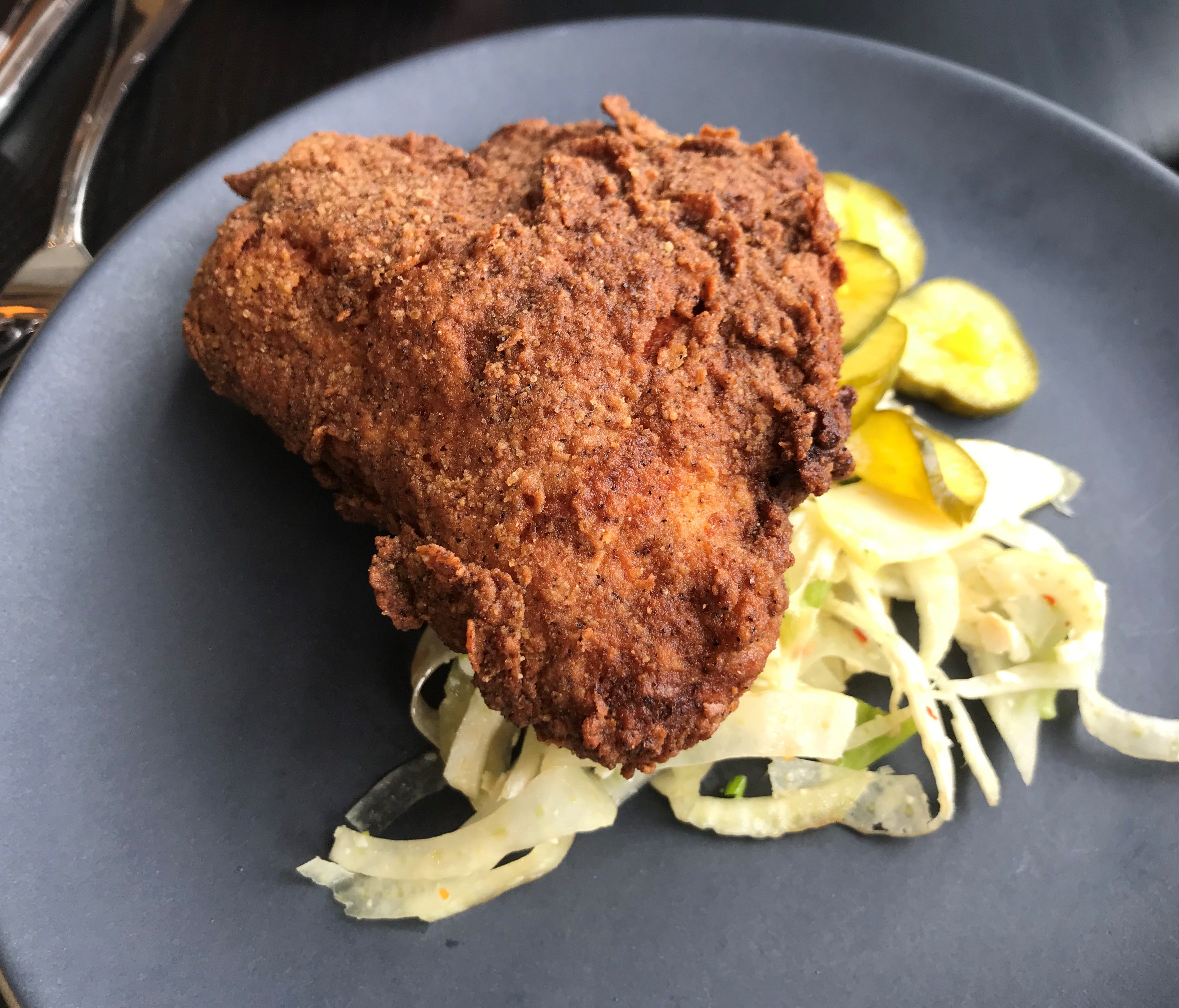 A fried chicken breast is served with house-made pickles and chunky coleslaw.