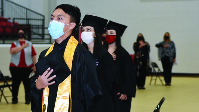 Xeng Yang, Faith Canada, and Hope Canada stand and recite, through masks, the Pledge of Allegiance during Friday's commencement cermony for the Class of 2020 held at Dimaondback Arena.