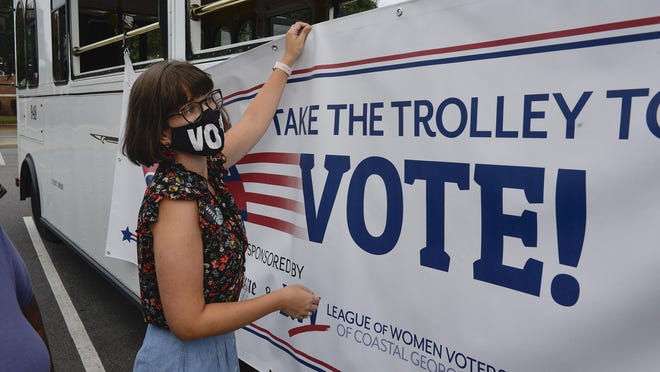 Eva Newbold hangs a sign on the side of a trolley announcing the League of Women Voters' of Coastal Georgia Take a Trolley to the Polls campaign.