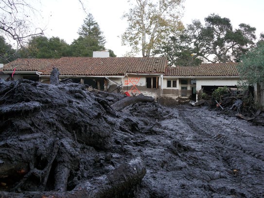 Mud and debris litter the front yard of a home in Montecito