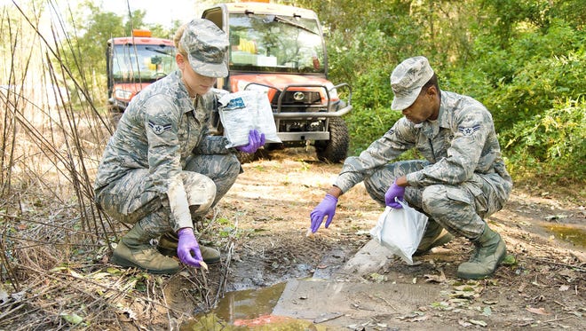 Airman 1st Class Jamie Tstinic, and Airman 1st Class Harry Landry, both 436th Civil Engineering Squadron pest control apprentices, prepare to place packets of VectoLex WSP into a puddle of standing water Thursday, in the Dover Family Housing area, Dover Air Force Base, Del. Tstinic, Landry and other members of the 436th CES Entomology section placed numerous 10-gram packets of VectoLex WSP, anywhere standing water was present that could possibly contain mosquito larva known to carry the West Nile Virus. 