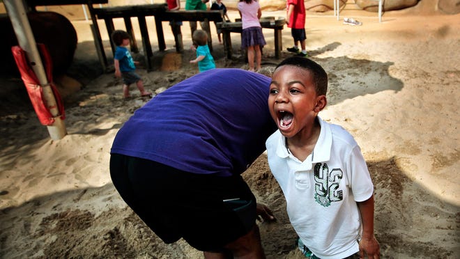 Alden Alexander, 9, lets out a bellow when he realizes how firmly he is planted after burying his legs in sand at the Woodland Discovery Playground at Shelby Farms in Memphis on Saturday. His grandfather Kwabena Ndubia, 62, stands at left.