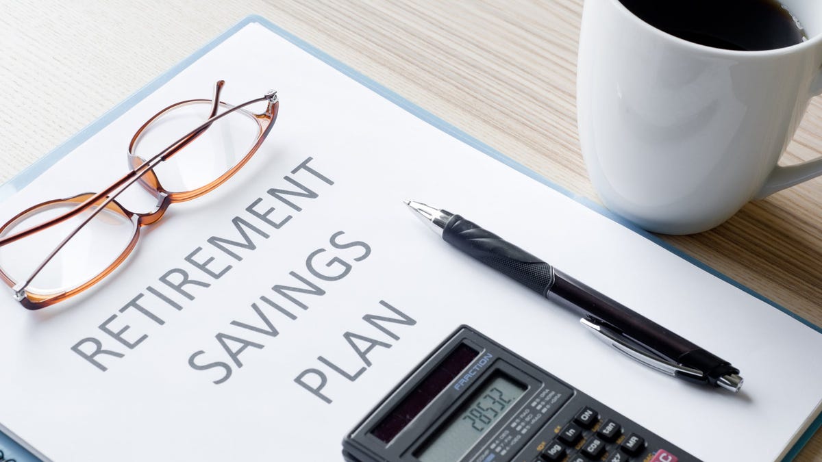 Eyeglasses, pen, and calculator resting on binder labeled retirement savings plan right next to a mug of coffee