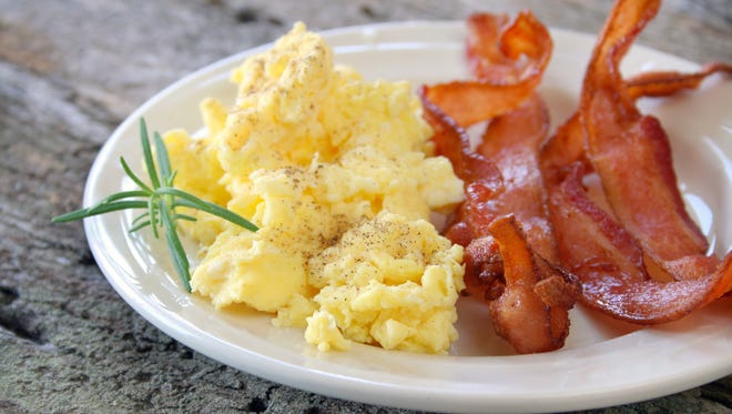 Scrambled eggs with crispy bacon on a plate, and garnished with a fresh sprig of Rosemary.