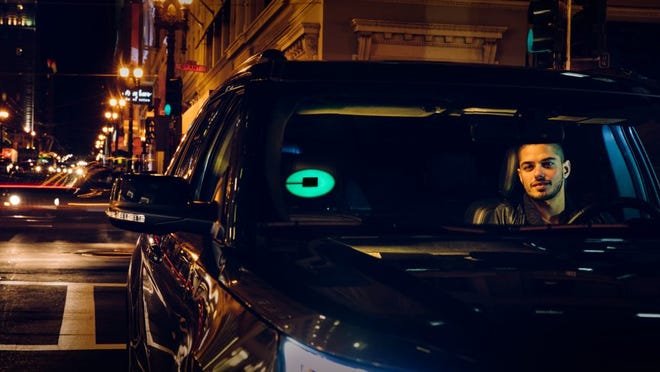 An Uber driver at night with an illuminated Uber beacon on the windshield.