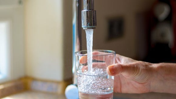 A hand filling a glass with water under a kitchen faucet.
