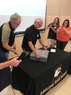 Royce Curtis, center, opens a 25-year-old time capsule while Brad Gallaway watches on Saturday in the Abilene High School cafeteria.