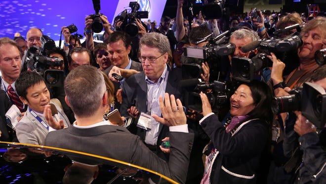 Volkswagen U.S. CEO Michael Horn, with his back to the camera,  raises his hands as he is surrounded by media after presenting at the 2015 Los Angeles Auto Show