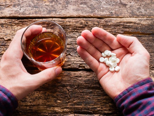 man holding a glass of alcohol and pills