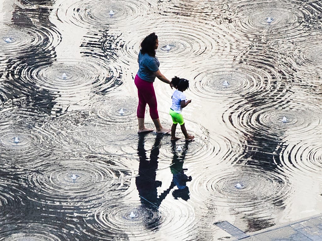 A woman and child walk through the cool water of a fountain on a warm spring afternoon at Dilworth Park in Philadelphia.