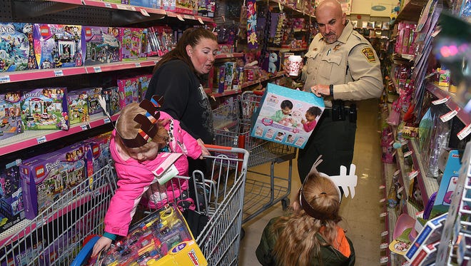 Deputy Jon Clark of the San Juan County Sheriff's Office helps Krystle Stalcup of Bloomfield and her two children, Haven Foster, 3, left, and Gloriana Foster, 4, right, shop for Christmas toys during Shop with a Cop on Saturday at Kmart.