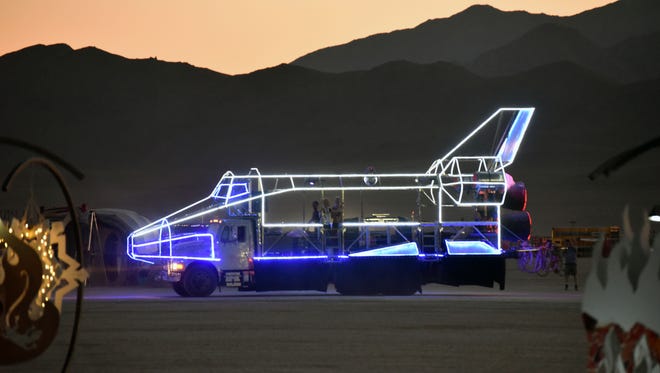 An illuminated vehicle resembling the Space Shuttle rolls across the desert at Burning Man.