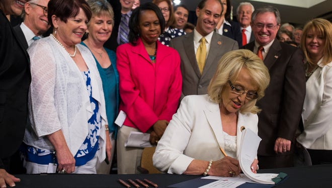 Gov. Jan Brewer signs Medicaid expansion legislation in 2103 as a bipartisan coalition looks on.