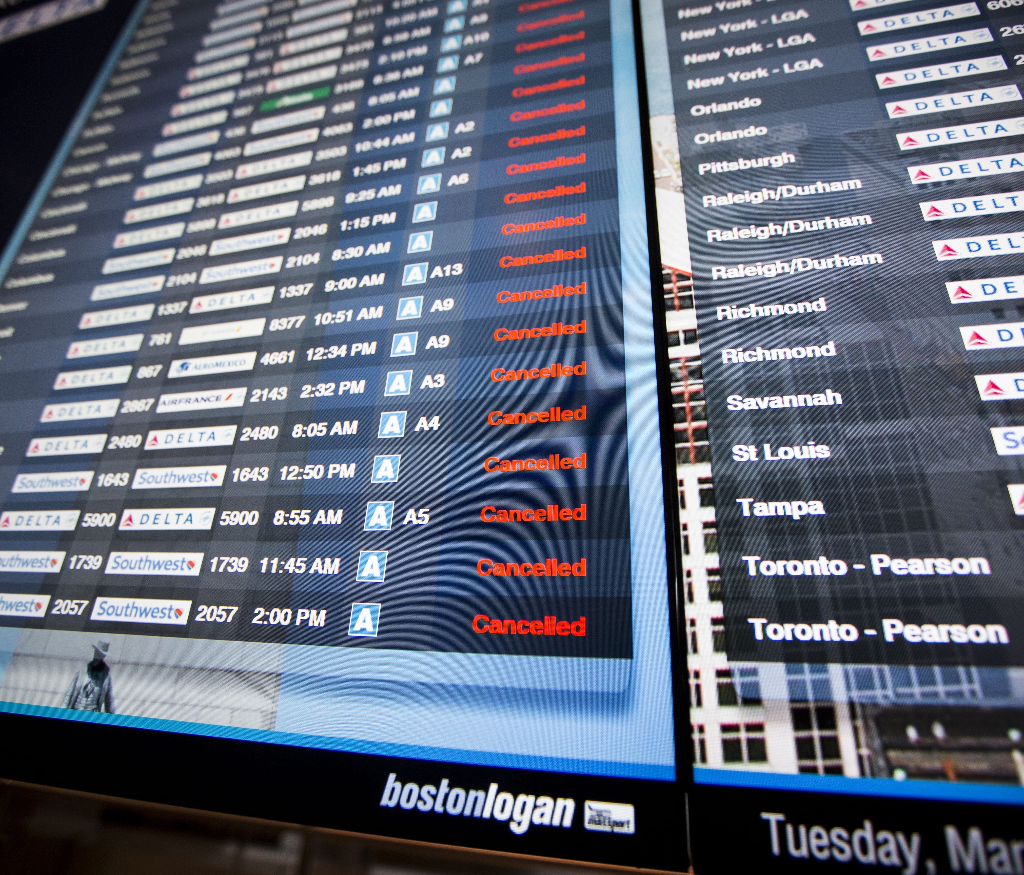 This file photo from March 13, 2018, shows a long list of cancellations on a flight information board at Boston Logan International Airport.