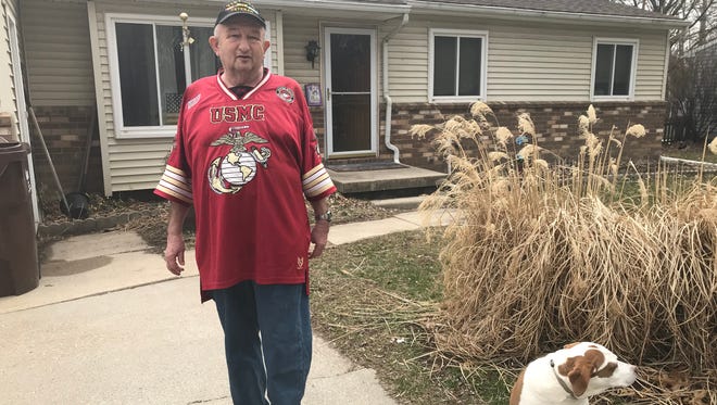 Colin Campbell, known as the Flag Man of Haslett, has a bad hip. Motorists are used to seeing him and his dog, Jayda, walking and waving a flag. He hopes to resume his role after upcoming hip surgery. Campbell and Jayda are in the front yard of their Haslett home April 9, 2018.