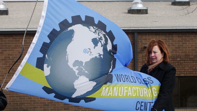 NEW Manufacturing Alliance coordinator Ann Franz steadies the special flag unveiled Friday March 27, 2015 at Lakeshore Technical College in Cleveland.