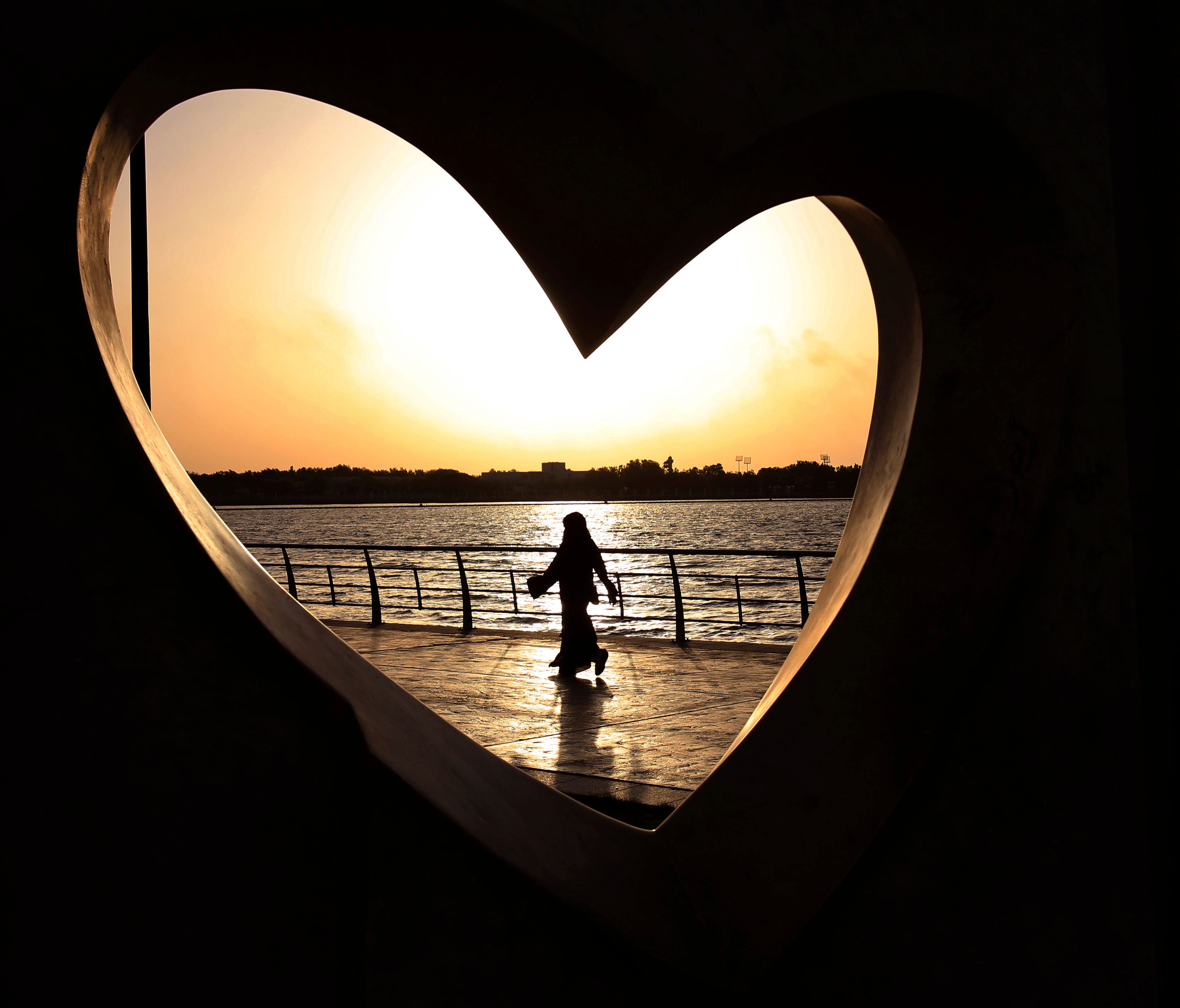 In this May 11, 2014 file photo, a Saudi woman seen through a heart-shaped statue walks along an inlet of the Red Sea in Jiddah, Saudi Arabia.