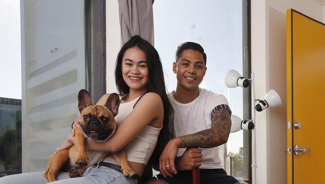 In this Wednesday, March 16, 2016, photo, Patrick Tupas, right, with his wife, Maria Real-Tupas, who is holding their dog Moon Moon Fitzgerald, sit in the living room at their shipping container apartment in Phoenix. “It doesn’t even feel like a shipping container. It’s also insulated really well,” said Patrick Tupas, who is in the Air Force. “It just feels like a regular apartment.”
