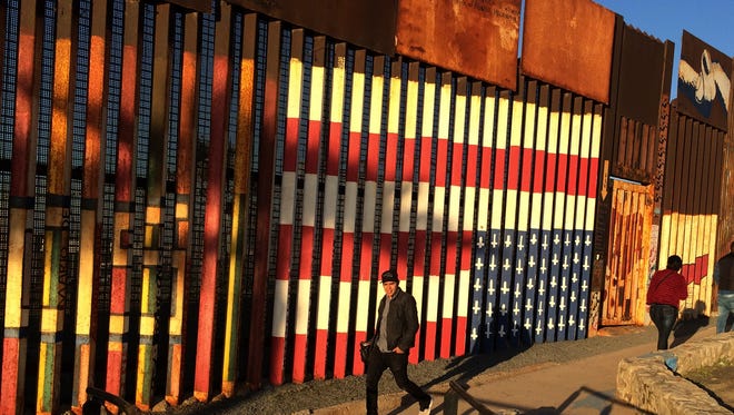 People pass graffiti along the border structure in Tijuana, Mexico, Wednesday, Jan. 25, 2017. President Donald Trump moved aggressively to tighten the nation's immigration controls Wednesday, signing executive actions to jumpstart construction of his promised U.S.-Mexico border wall and cut federal grants for immigrant-protecting "sanctuary cities." (AP Photo/Julie Watson)
