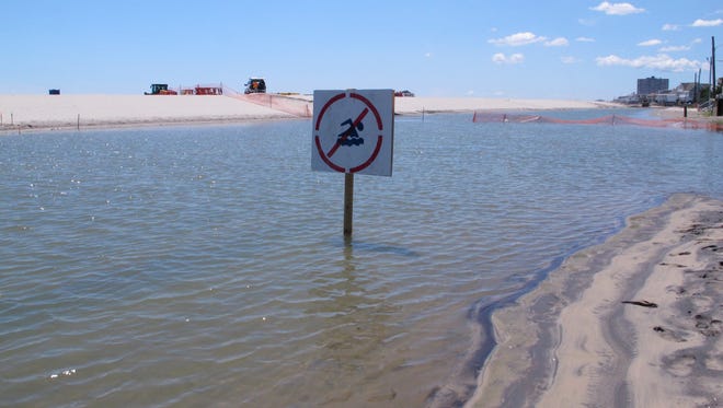 This July 31, 2017 photo shows a no swimming sign in one of numerous large pools of water that have formed on the beach in Margate N.J. due to heavy rains.