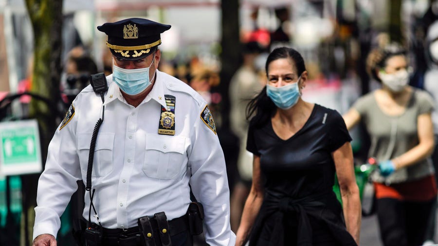 A police officer wears a protective mask as he walks among people at the Union Square GreenMarket on Saturday in New York.