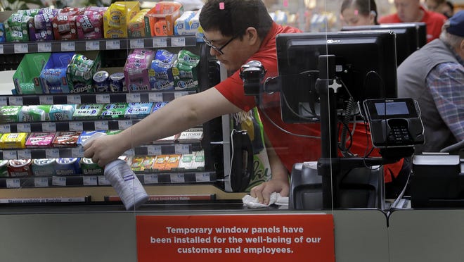 FILE - In this March 26, 2020, file photo, Garrett Ward sprays disinfectant on a conveyor belt between checking out shoppers behind a plexiglass panel at a Hy-Vee grocery store in Overland Park, Kan. From South Africa to Italy to the U.S., grocery workers â many in low-wage jobs â are manning the front lines amid worldwide lockdowns, their work deemed essential to keep food and critical goods flowing. (AP Photo/Charlie Riedel, File)