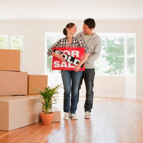 Couple holding sold real estate sign next to movin