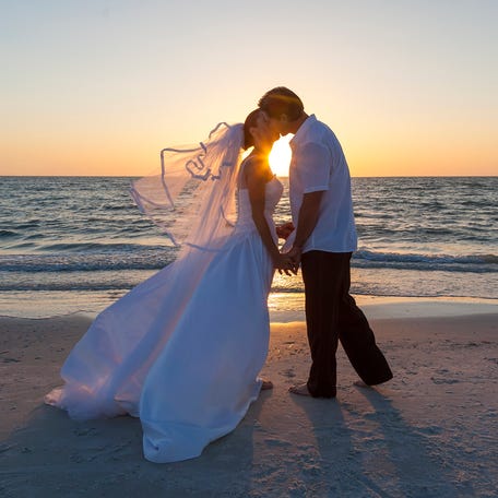 A married couple, bride and groom, kissing at sunset or sunrise on a beautiful tropical beach