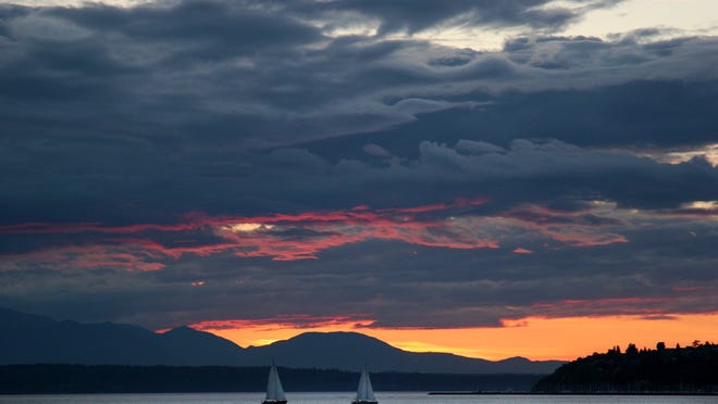 A pair of sailboats head towards Seattle on Elliott Bay, with Bainbridge Island in the background at sunset. King County is set to pay over $5 million to settle a threatened lawsuit from the Suquamish Tribe over sewage spills that have overflowed into Puget Sound.