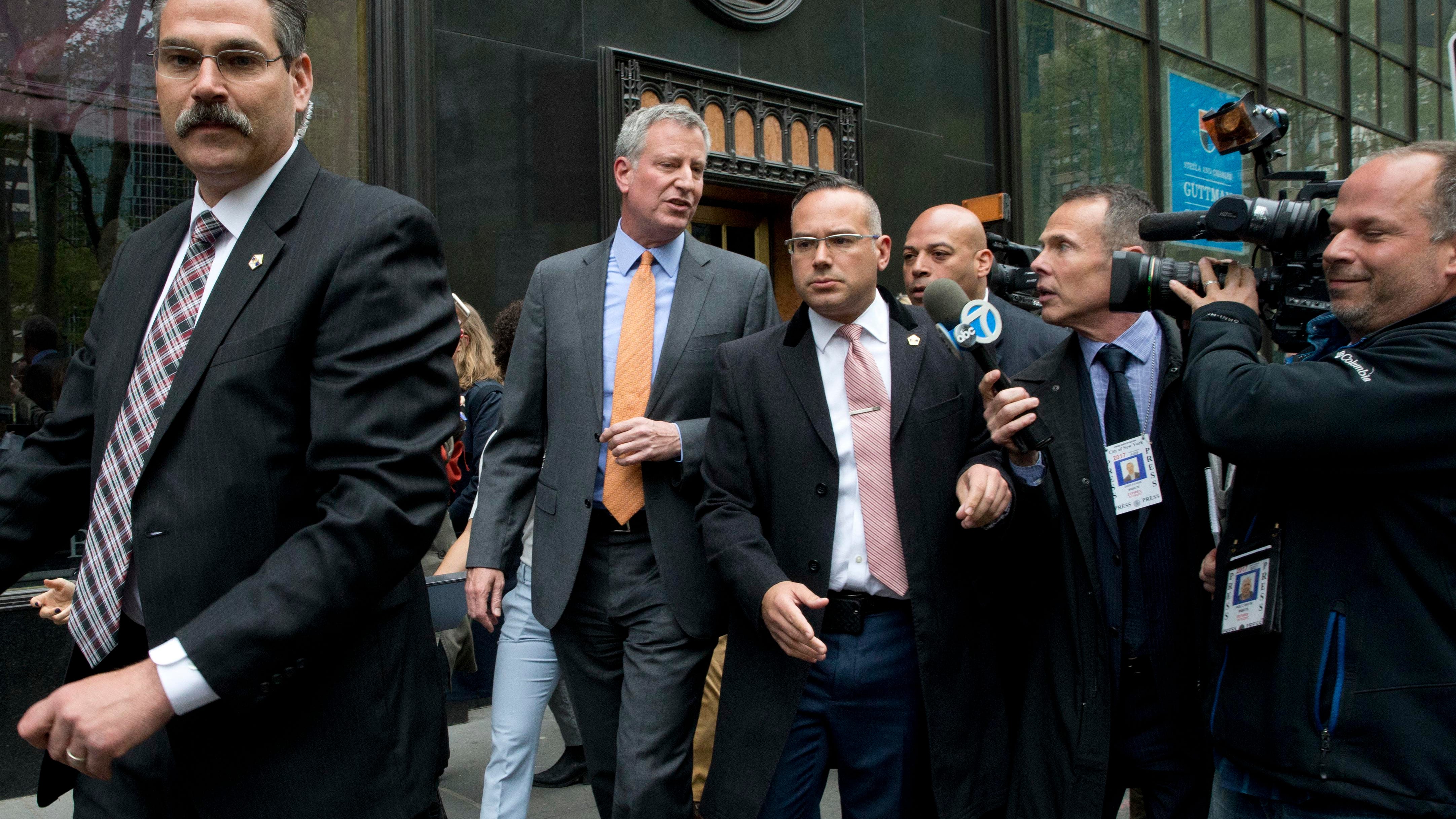 New York City Mayor Bill de Blasio, second from left, is surrounded by security and followed by reporters as he leaves an event April 28, 2016, in New York.